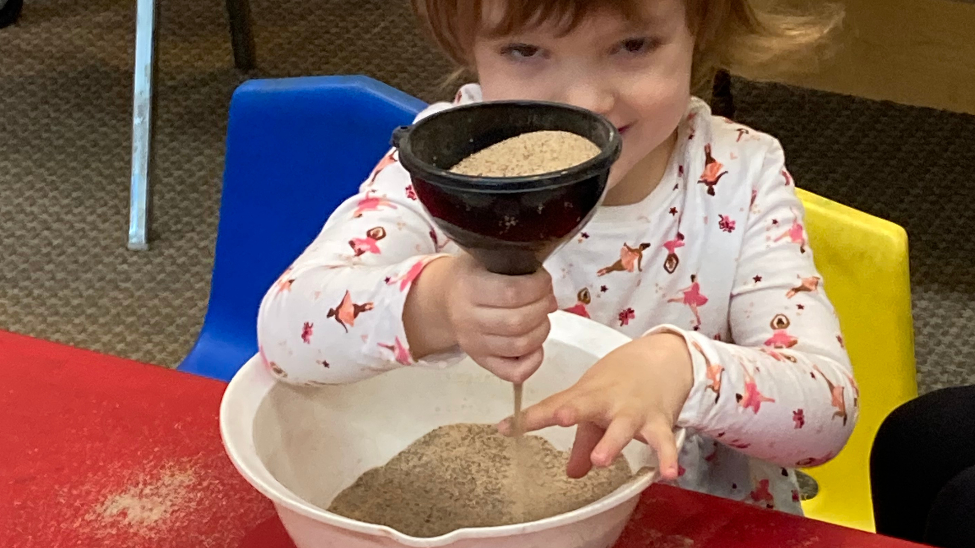 young girl holding funnel that has sand flowing through it